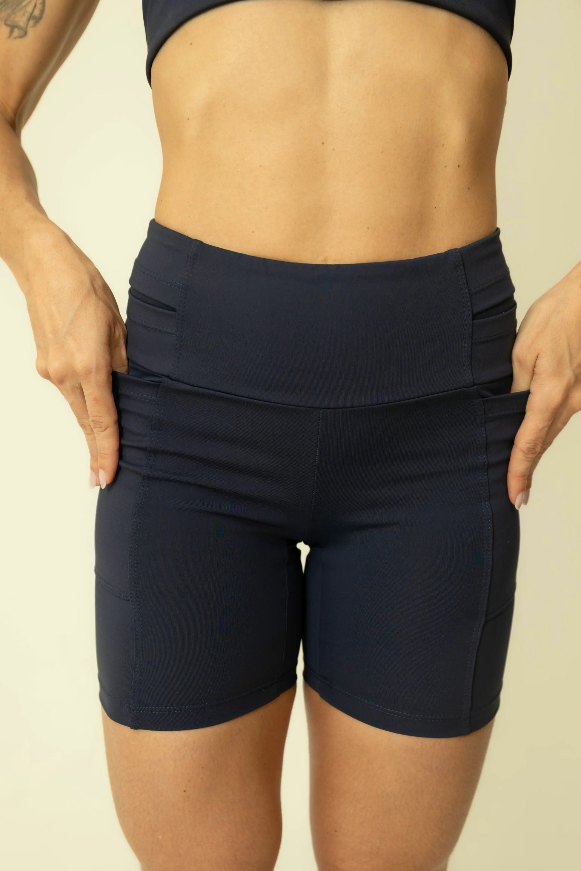 Detailed studio shot of a woman demonstrating the elastic waistband of the Caravela Blue high-waisted running shorts by Tempus Own, highlighting the firm compression and secure fit.