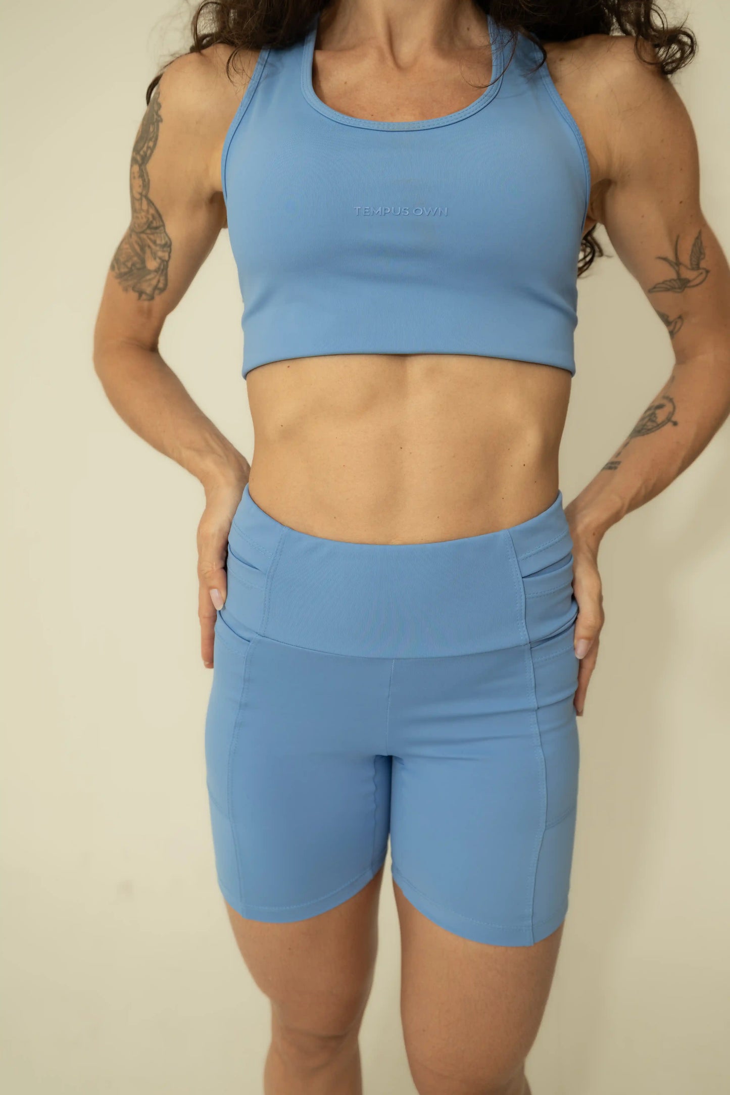 Front view of a woman wearing a Caravela Blue running set, featuring a supportive sports bra and high-waisted shorts with pockets.